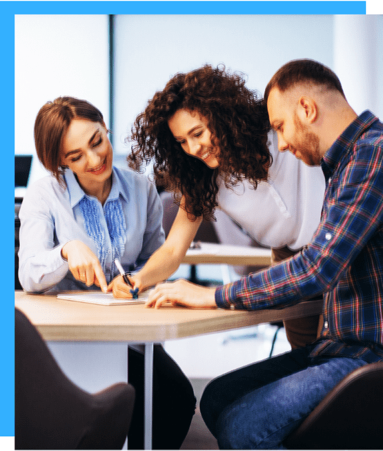 Clickable Image of two corporate females and one male seated on a work table together. 